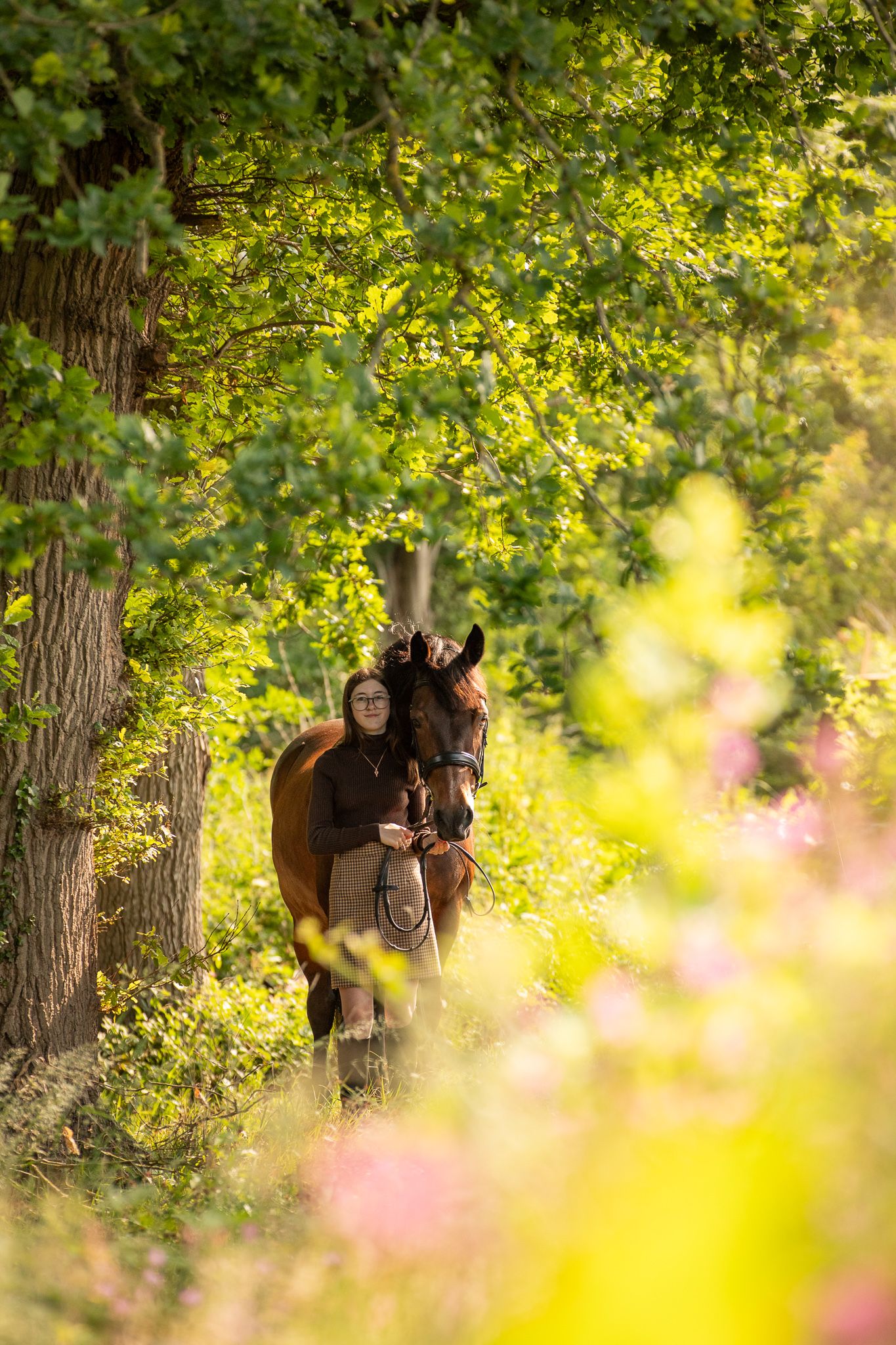 A brown horse and person stand together in a woodland clearing filled with blooming bluebells.