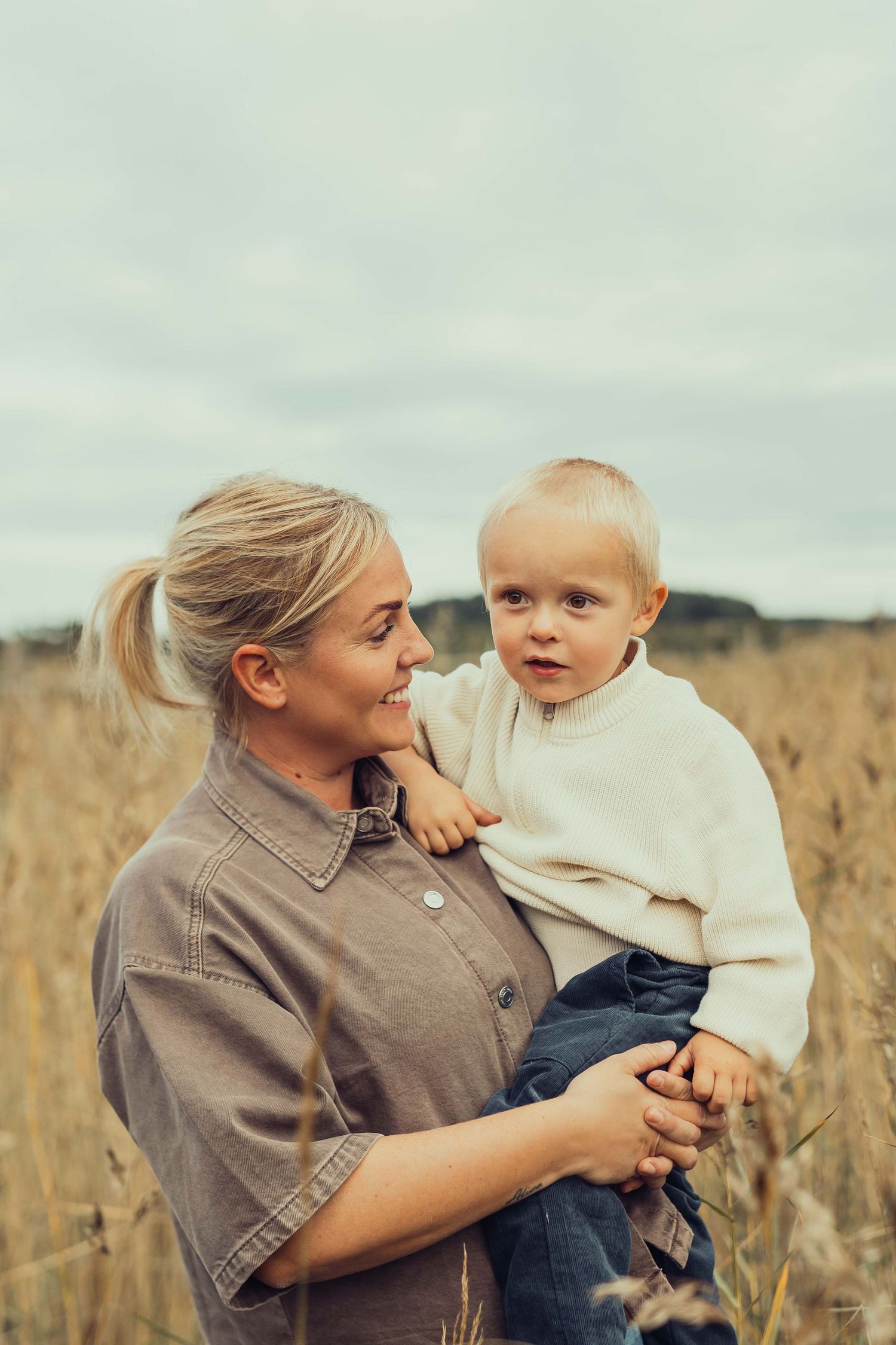 Mamman Frida med sonen Alfons på höften står bland vassen vid havet