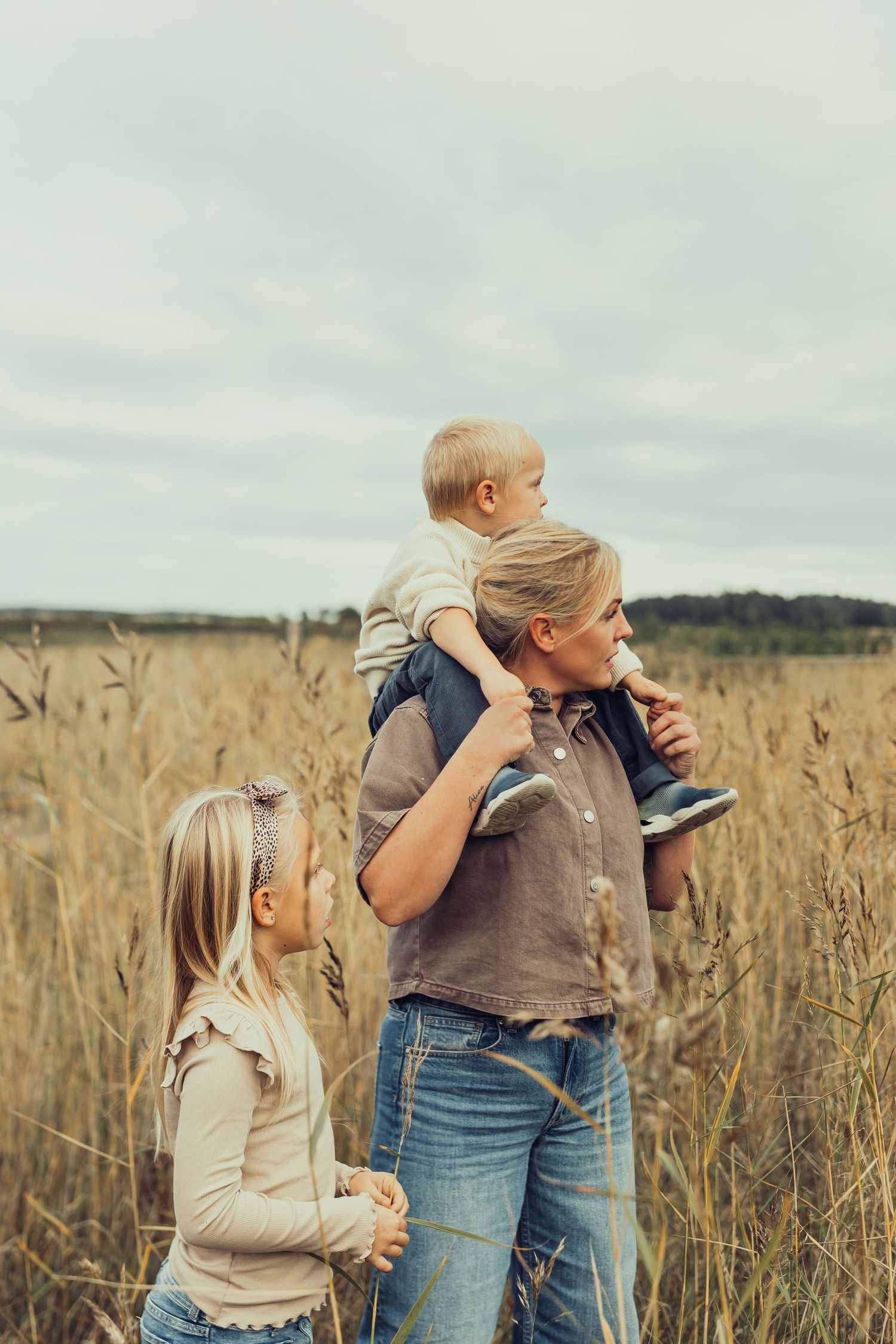 En mamma har sin son på axlarna och blickar ut mot havet, hon står bland vassen med sin dotter bredvid sig nedanför