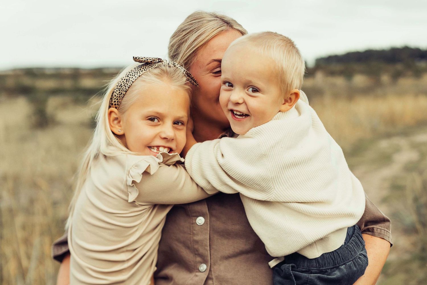 Busig naturlig bild på två barn som leker med sin mamma och tittar in i kameran