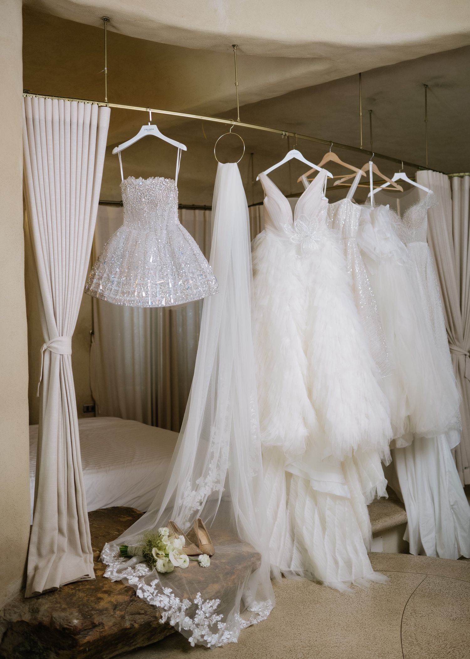 Collection of white bridal gowns hanging in a dressing room with tulle and lace details.