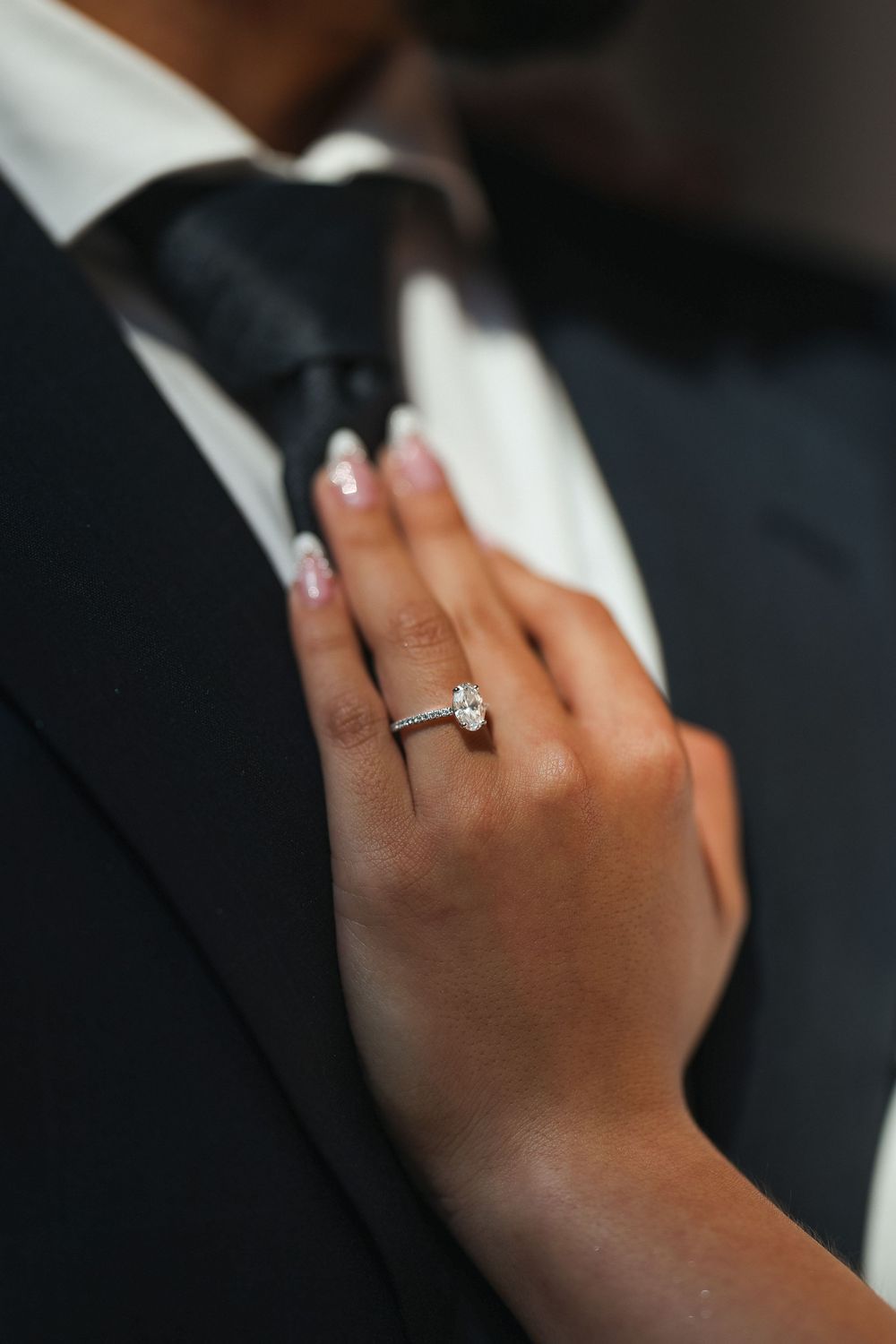 Close-up of engagement ring on hand against formal black attire background.