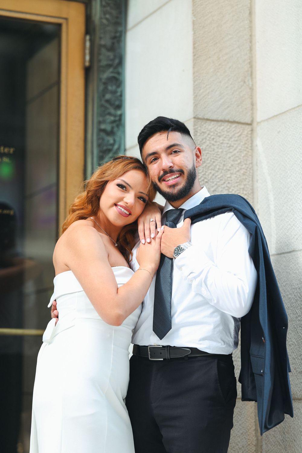 Casual wedding portraits against a light stone wall showing playful interactions.