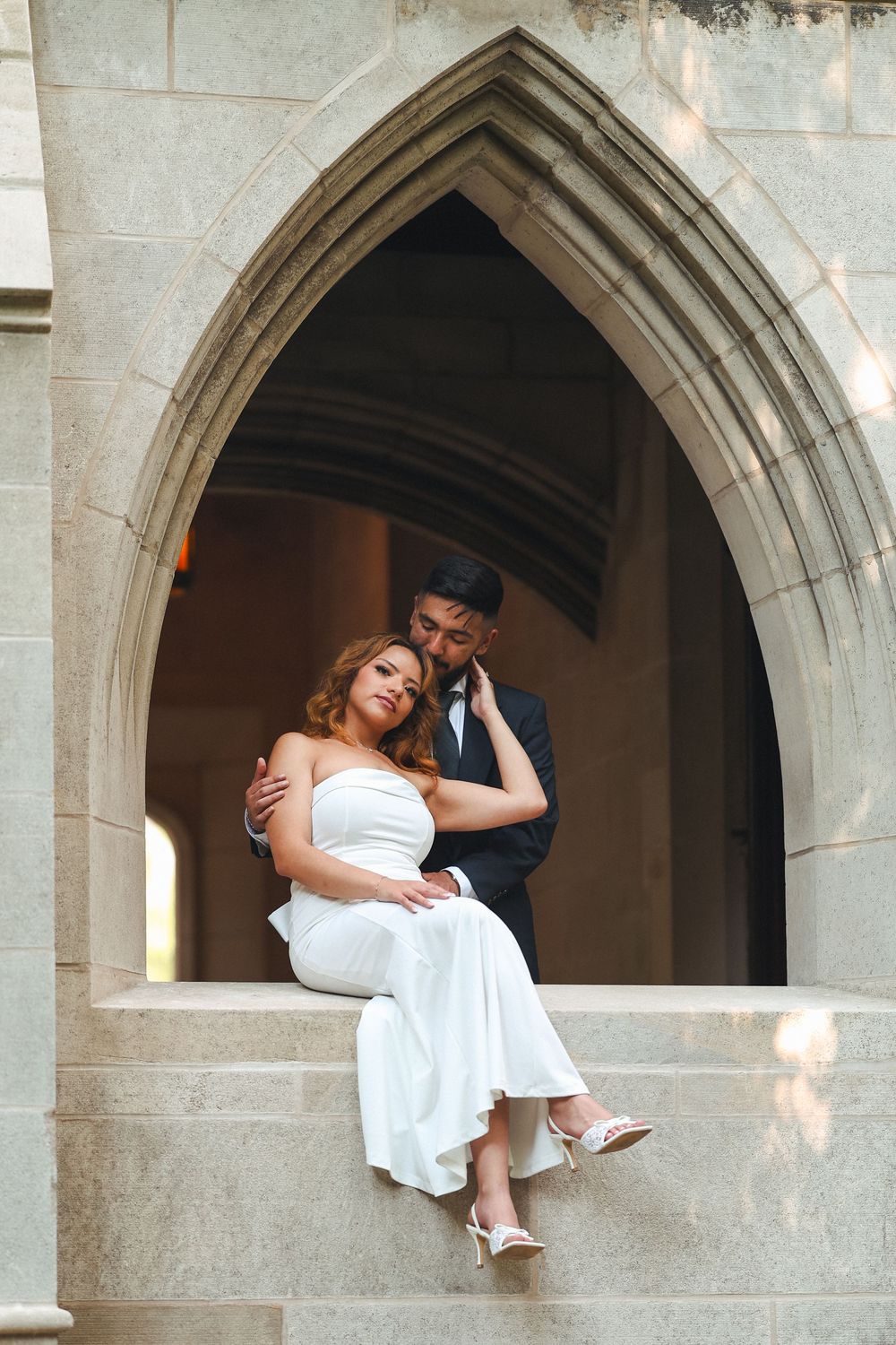 Bride and groom pose playfully in stone archway during wedding photoshoot.