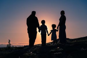 Silhouette of family of four holding hands at sunset on rocky hilltop.