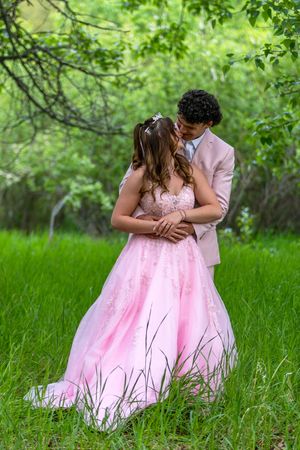 Couple in prom attire sharing a romantic moment in a lush green forest setting.