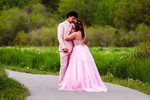 Young couple in pink prom dress and tan suit dancing on a garden pathway.