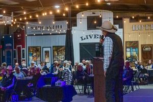 Cowboy hat speaker presenting at podium in western-themed venue with string lights overhead.