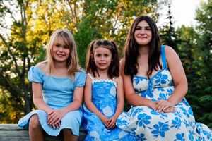 Three girls in blue dresses sitting together outdoors with green trees in the background.