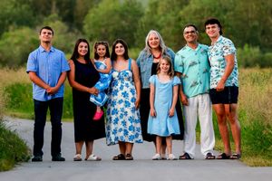 Family of nine posing together on a path surrounded by lush green trees during a warm summer evening.