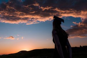 Silhouette of a person wearing a hat standing against a vibrant sunset sky with dramatic clouds.
