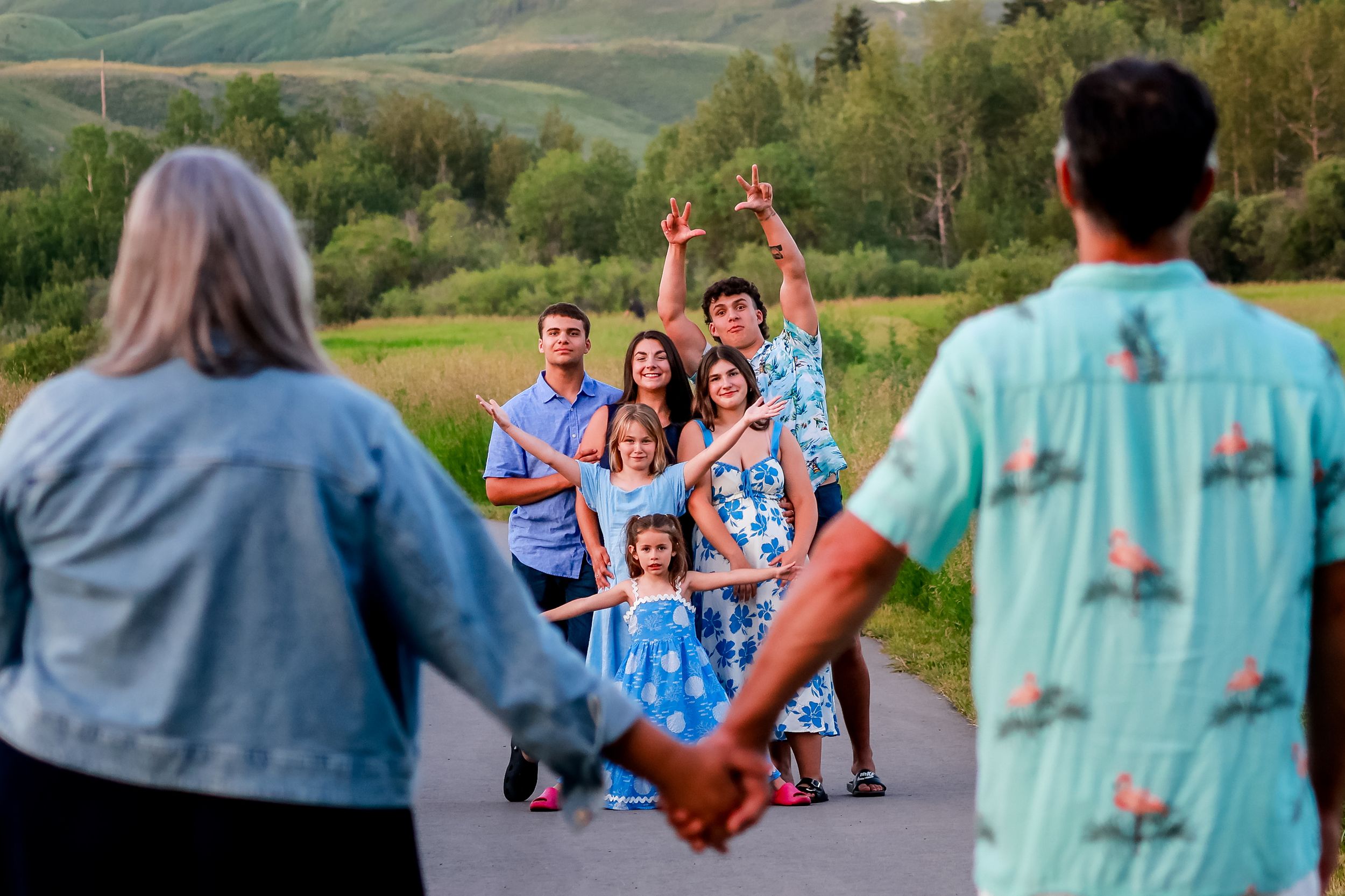 Family group holding hands on a road with green hills, smiling and posing for a photo outdoors.