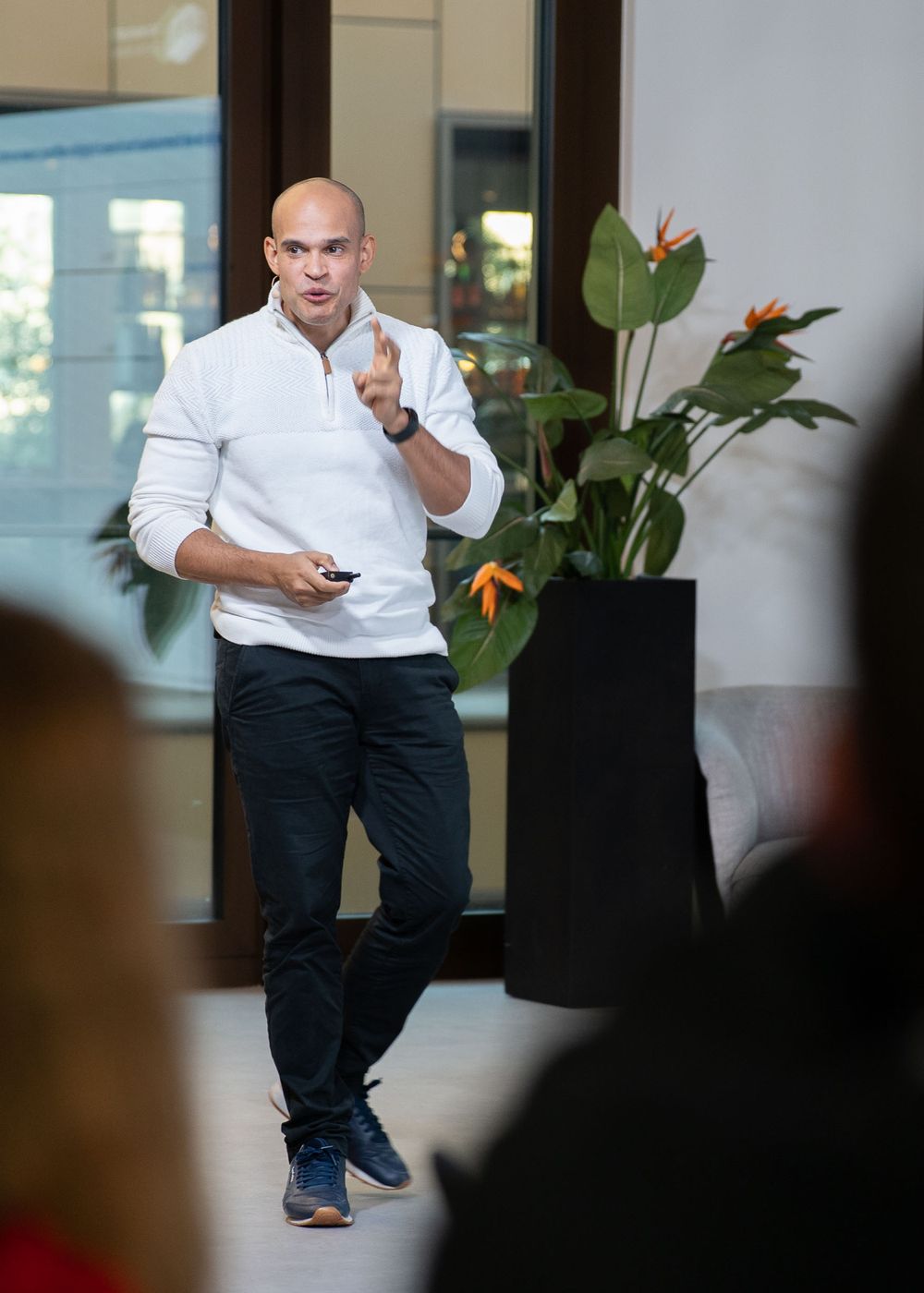 Executive presenting in a business environment wearing white dress shirt and dark pants beside a large decorative plant.
