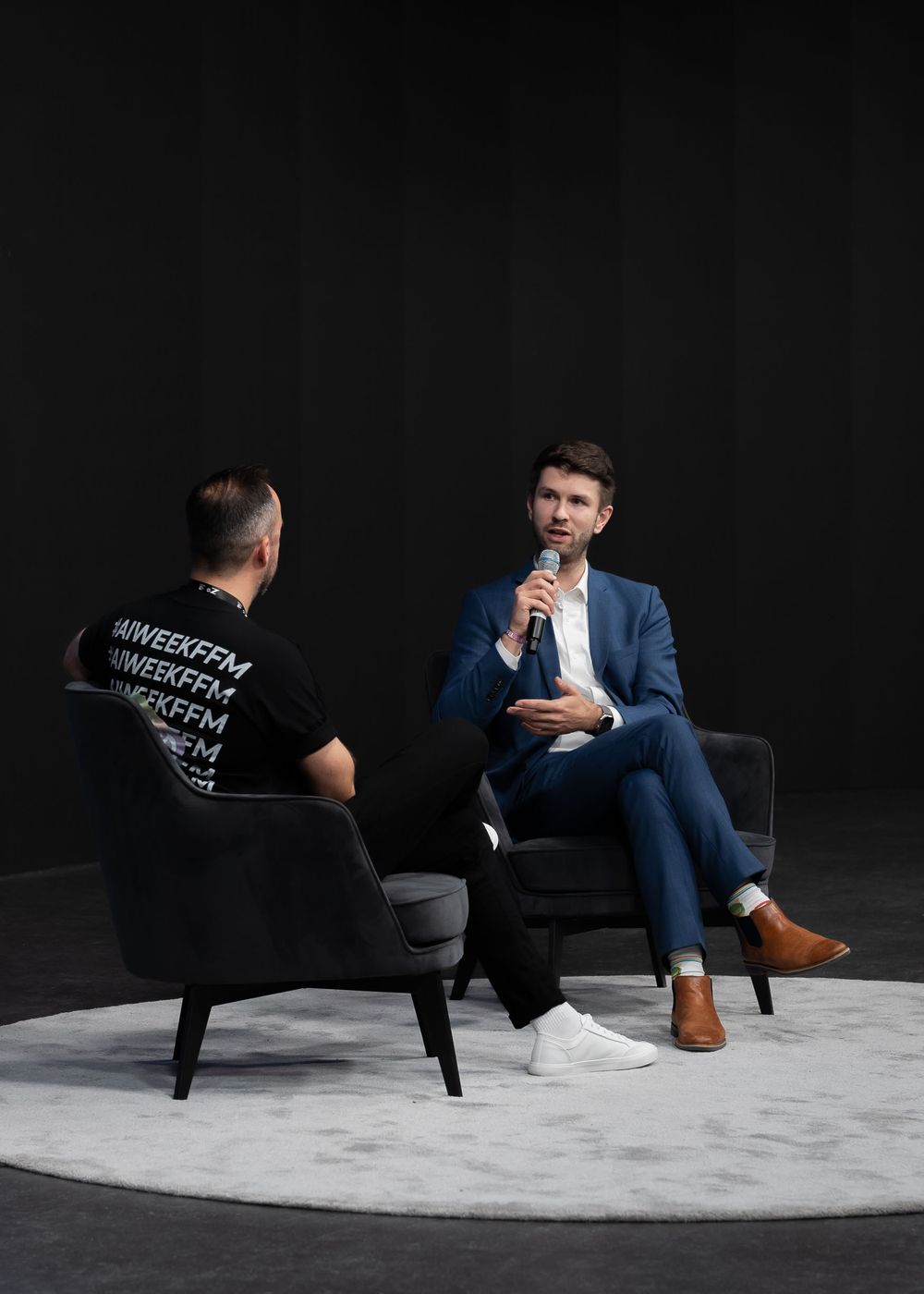 Two people having a professional conversation while seated in modern armchairs against a dark background.