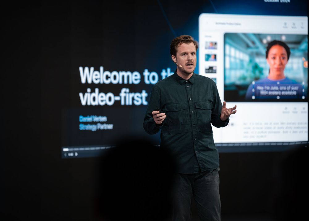 Professional speaker on stage presenting at a tech conference in front of digital screens and displays.