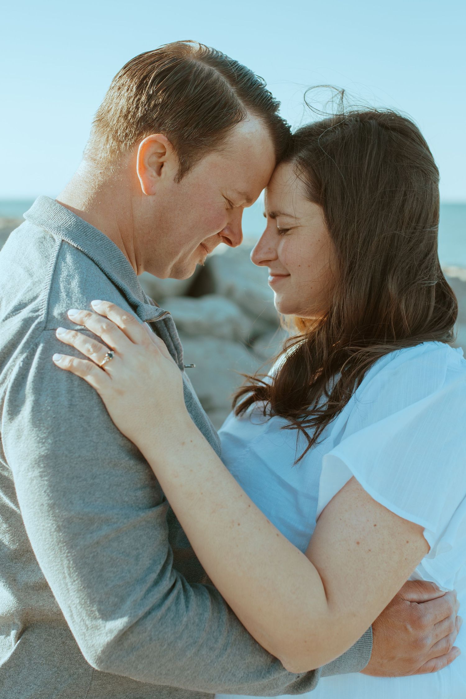 Couple embracing tenderly against a bright blue sky background.