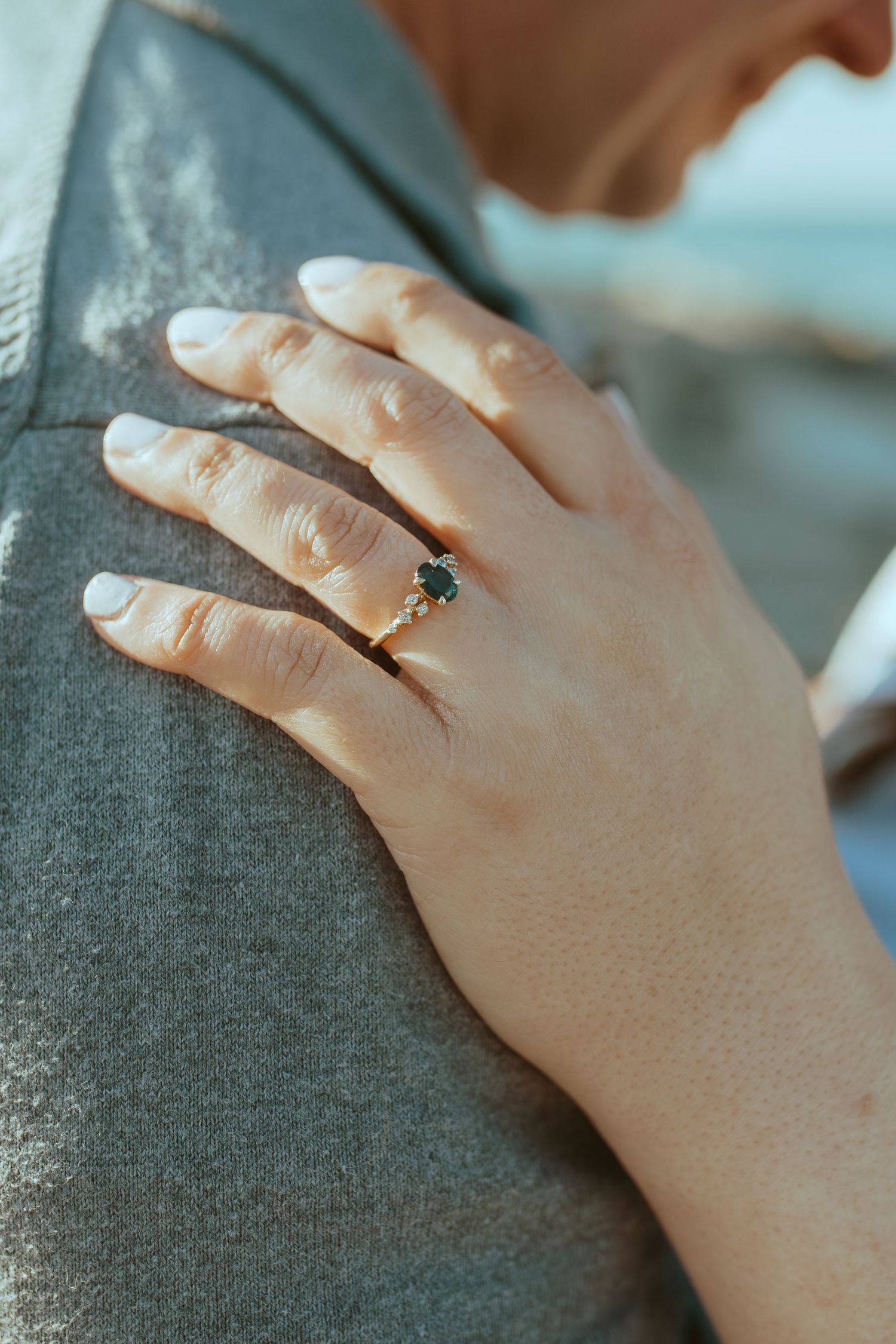 Close-up of hands with an engagement ring resting on grey fabric, showing a tender moment.