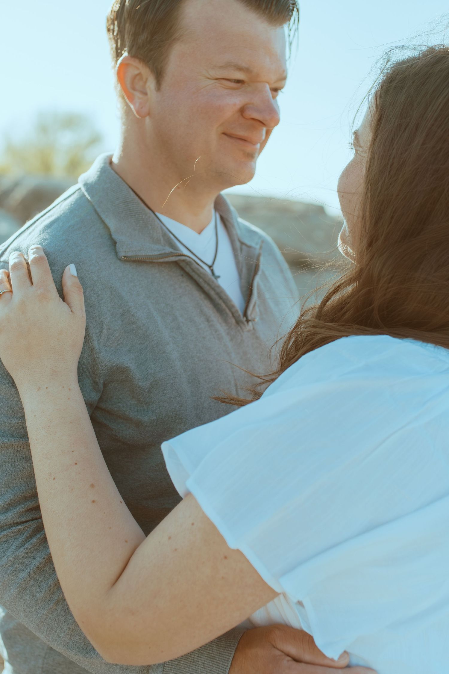 Close up shot of a couple in a tender embrace with one wearing gray and one in white.