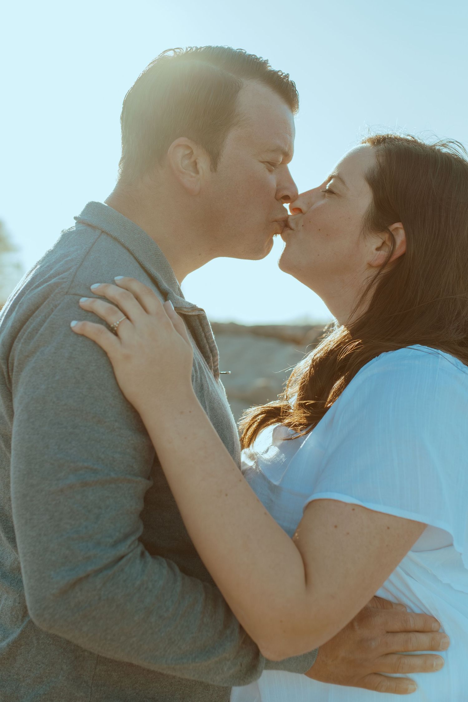 Intimate moment between a couple in white and grey clothing against bright sky.