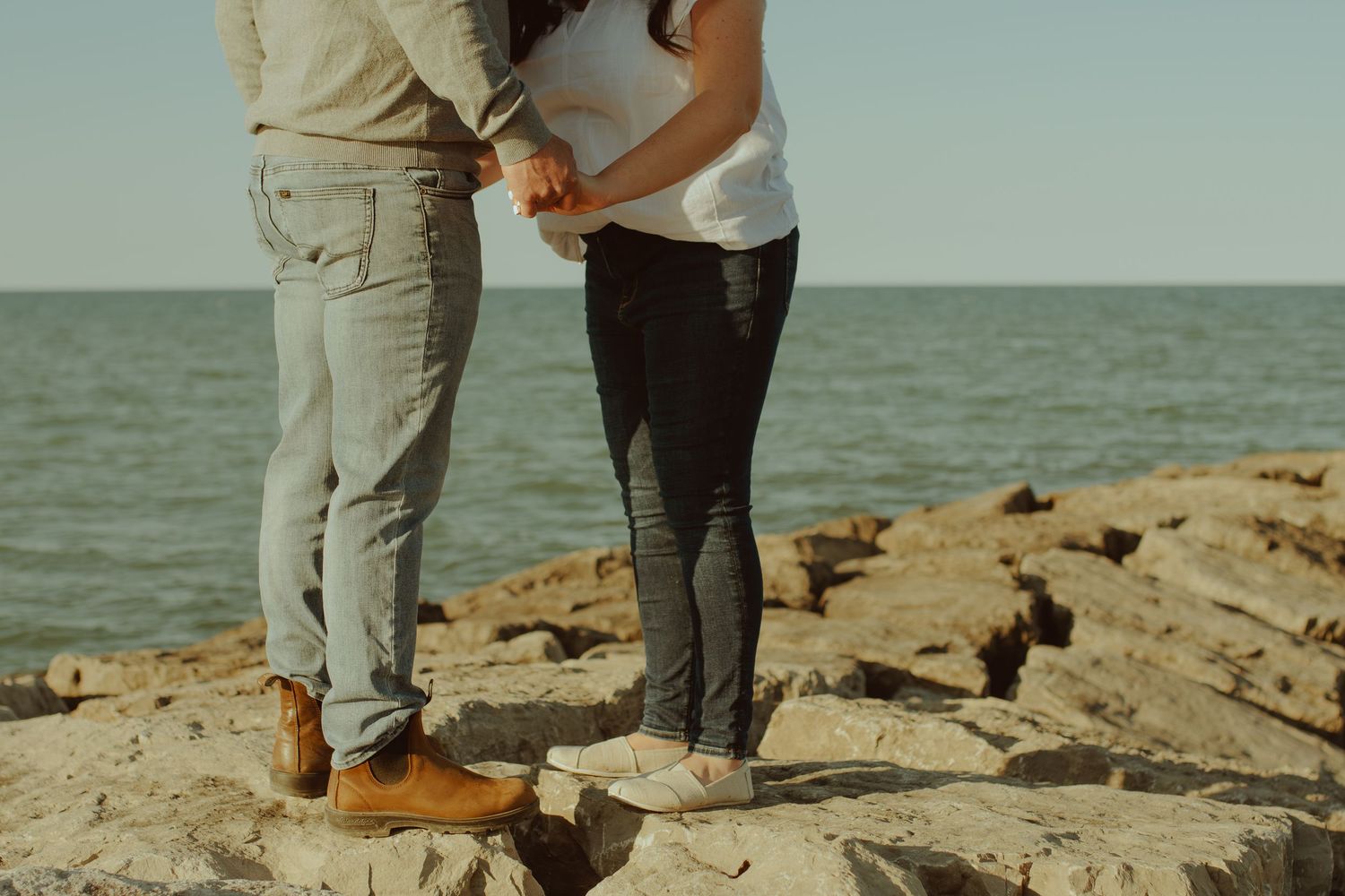 A couple stands close together on rocky coastal terrain overlooking a misty ocean view.