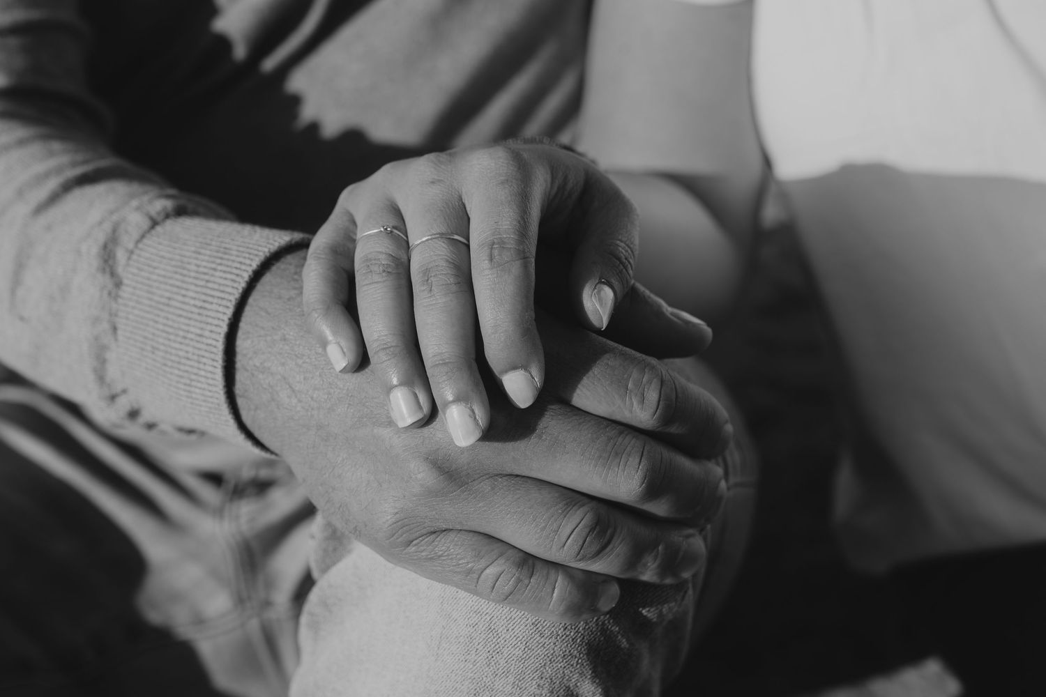 Two hands clasped together in black and white, showing an intimate emotional connection between people.