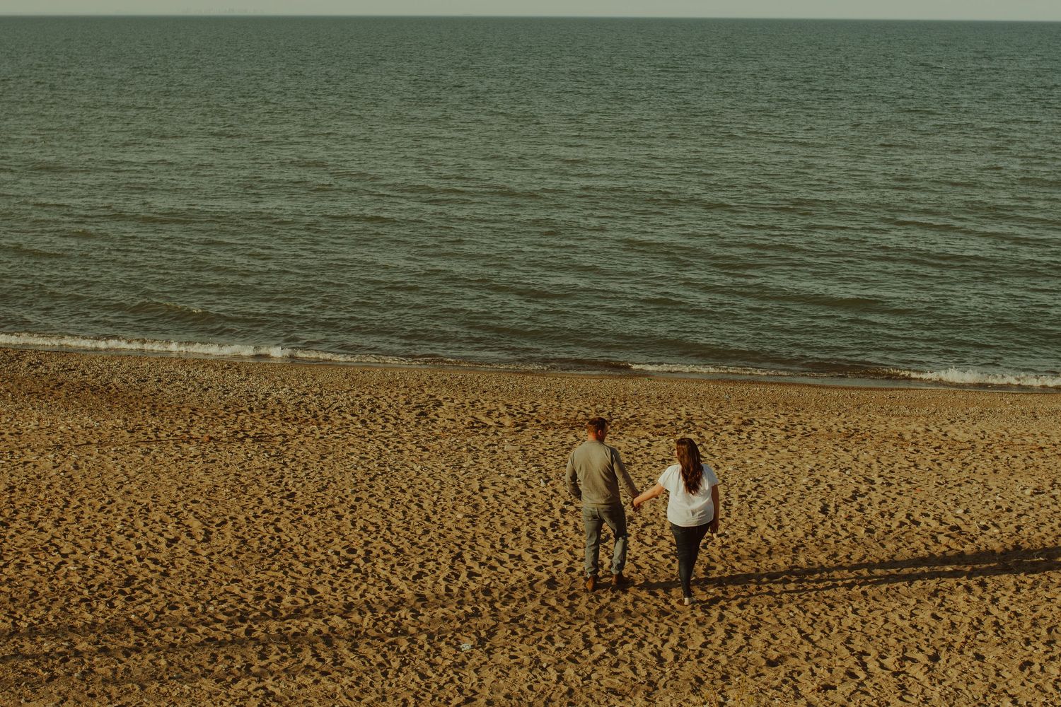 A sandy beach stretches into the distance with calm ocean waters and blue sky in view.
