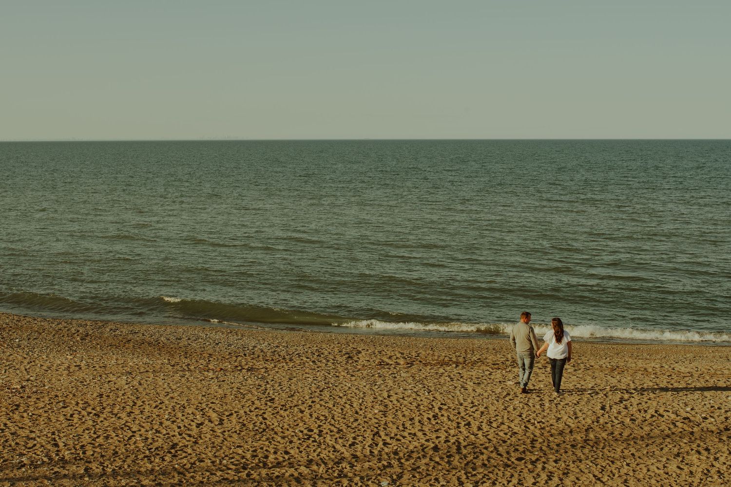 Two people stroll together on a peaceful sandy beach during golden hour.