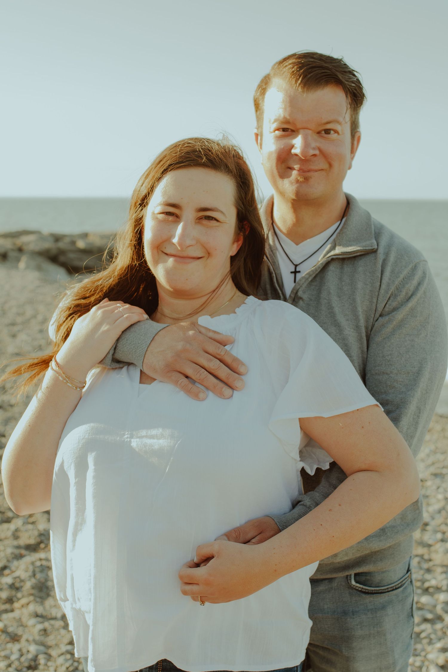 A couple poses playfully together on a rocky beach during a sunny afternoon photoshoot.
