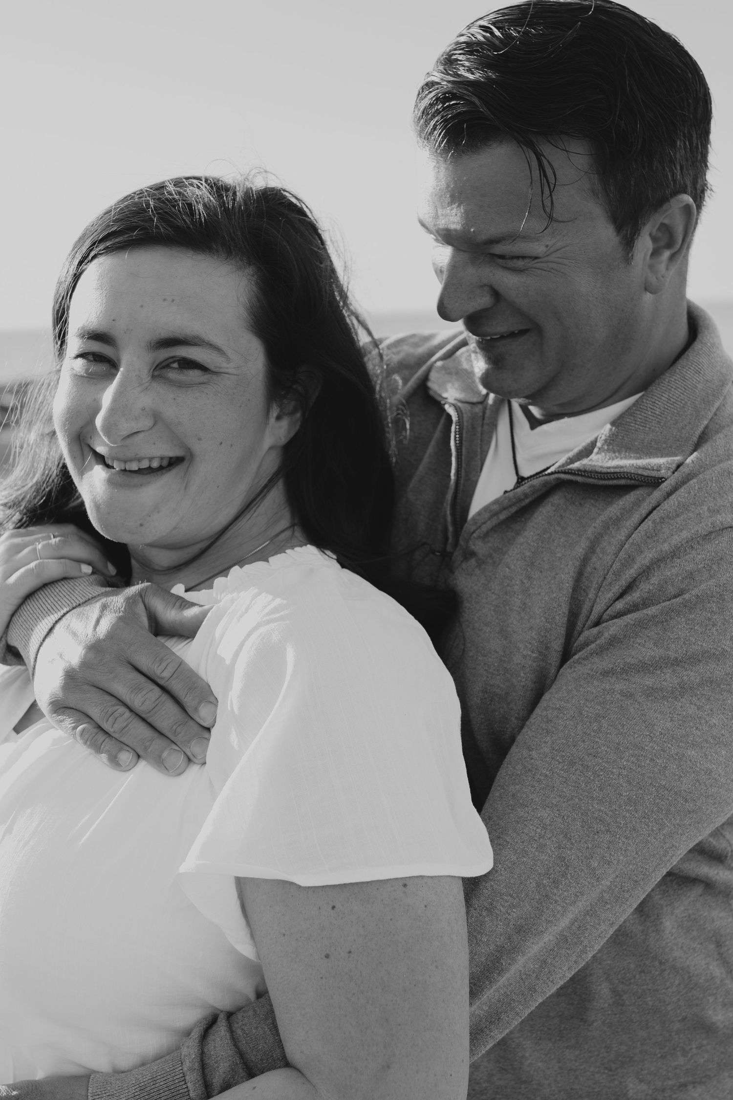 A black and white photo captures intimate candid moments between a couple on a beach.