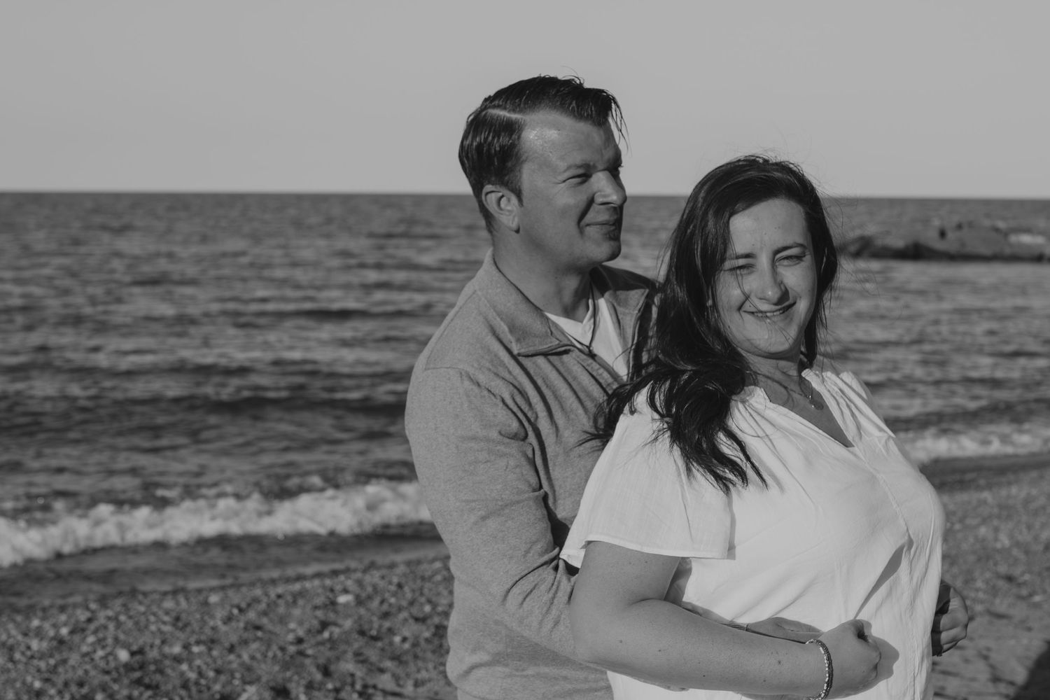 A black and white photo captures a sweet romantic moment between a couple at the beach.