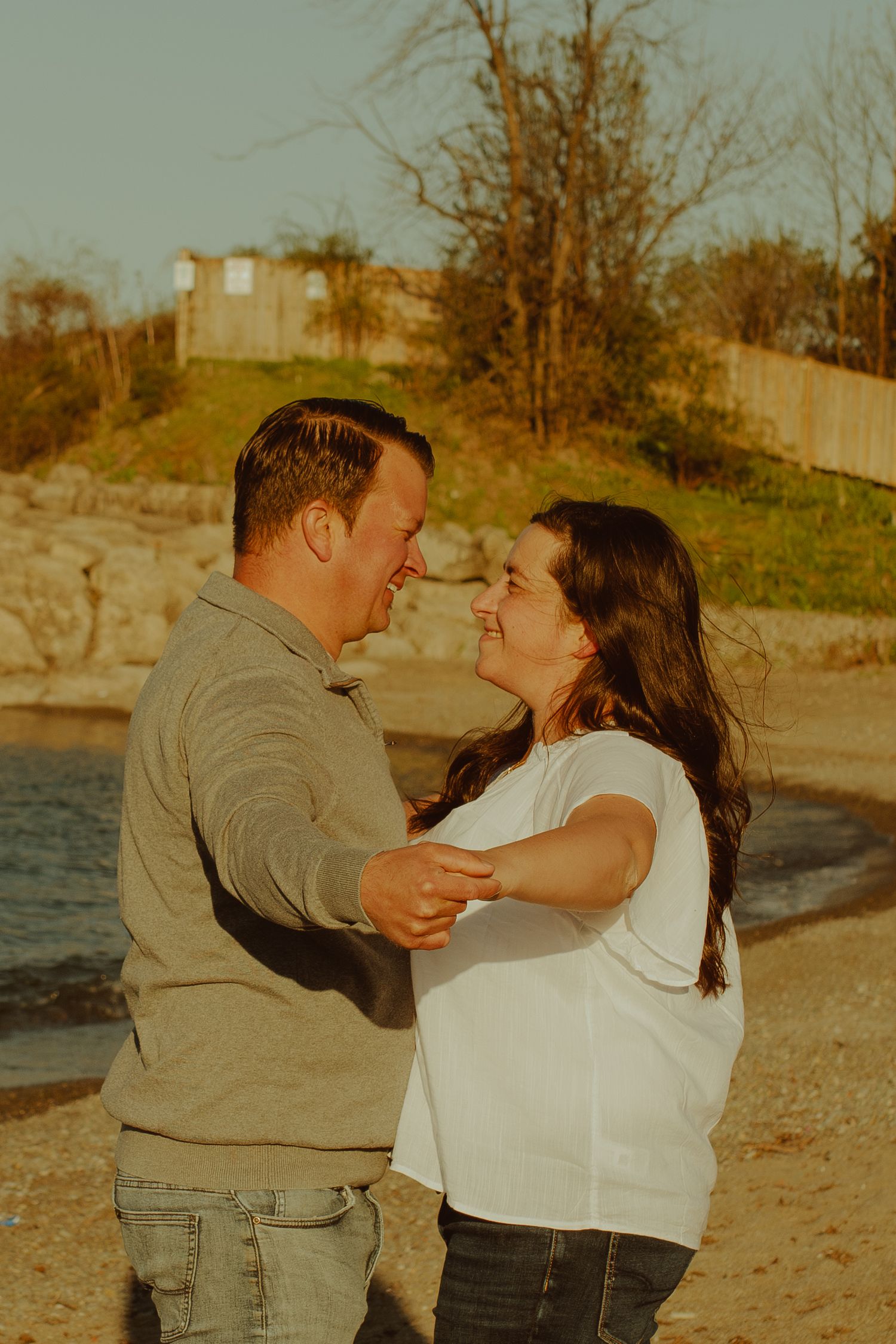 A couple shares a joyful moment during their sunset beach photoshoot in warm lighting.