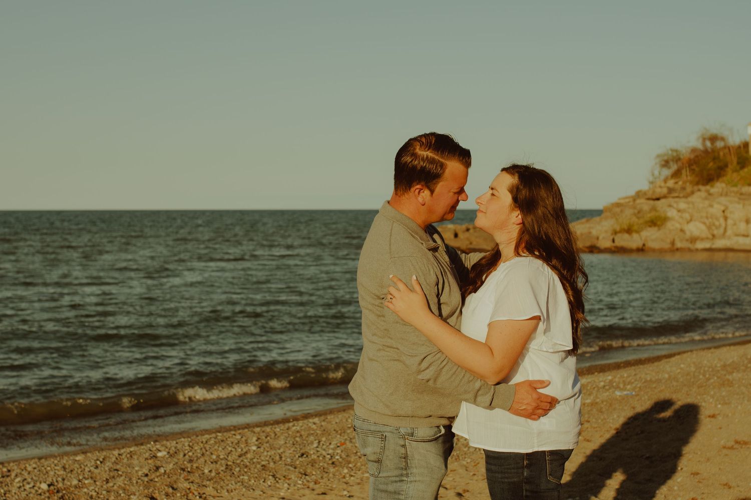 A couple embraces on the beach at sunset with the ocean waves in the background.
