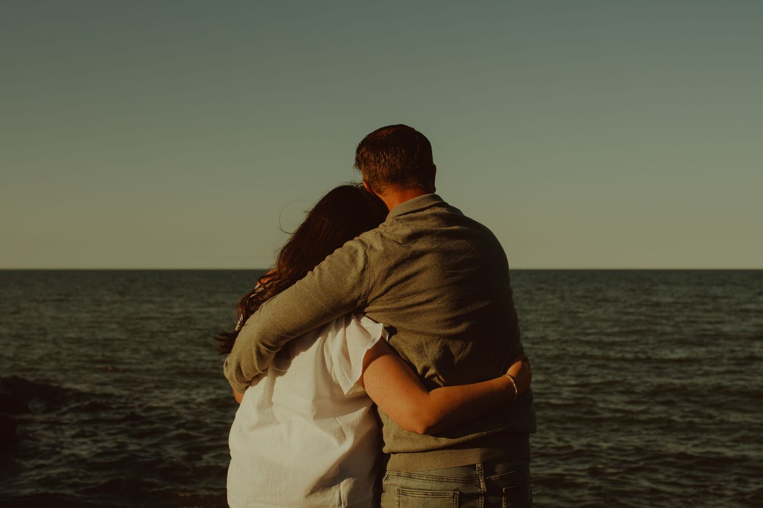 Silhouettes of a couple embracing against a moody ocean backdrop during golden hour.