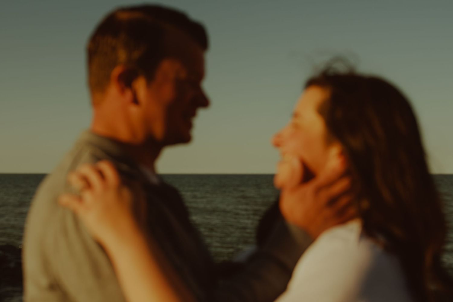 Silhouetted couple sharing a romantic moment at sunset by the ocean.