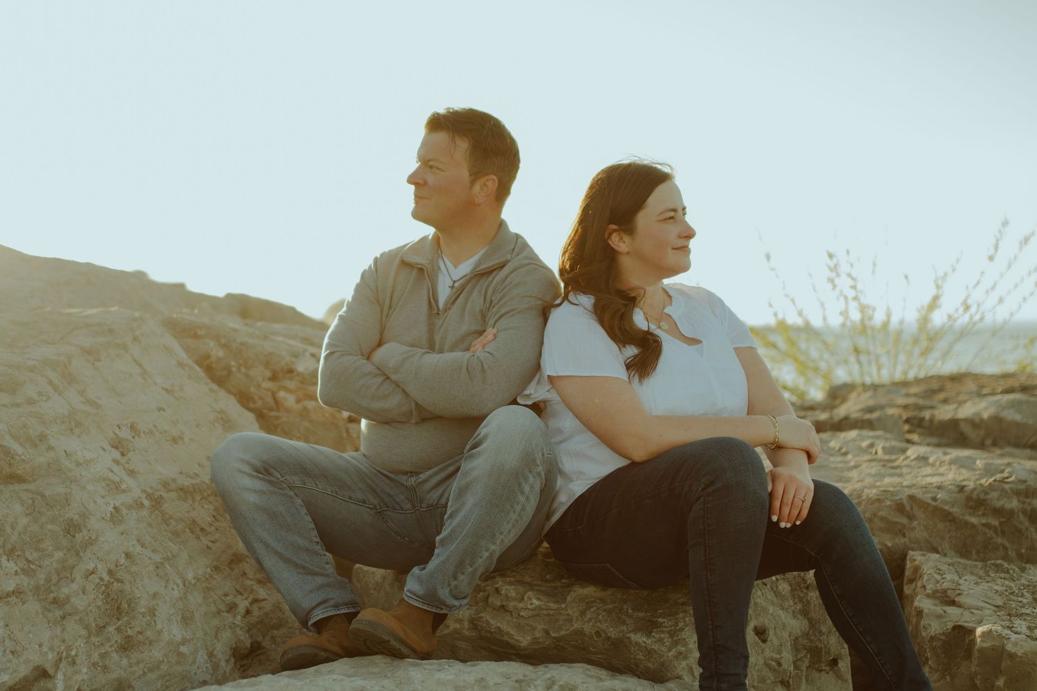 A couple sits back to back on coastal rocks during a moody afternoon.