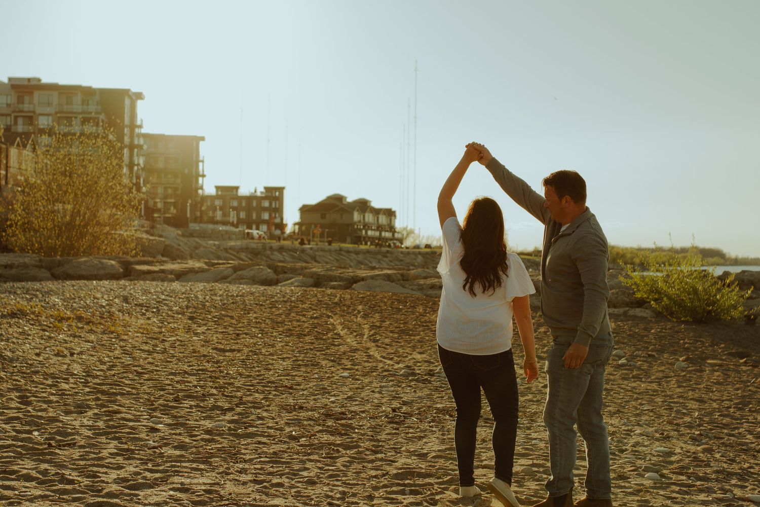 Two people walking hand in hand on rocky beach during sunset.
