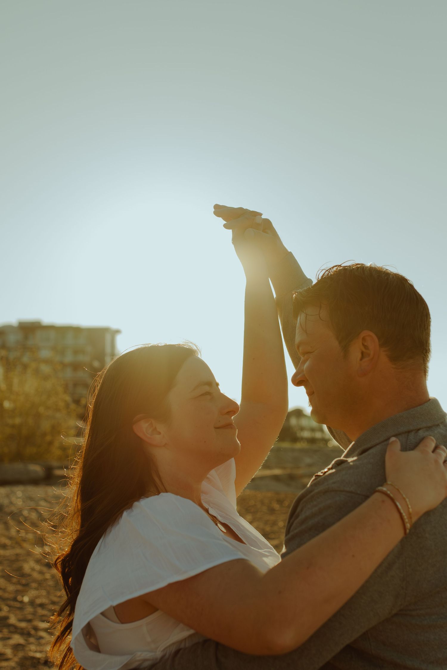 A backlit couple shares an intimate embrace on the beach during sunset with golden light streaming through.