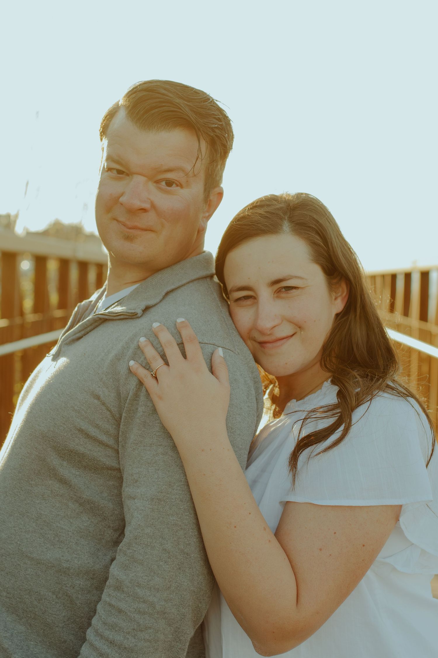 A romantic couple embraces outdoors as the warm sunlight casts a golden glow during their photoshoot.