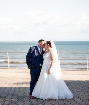 A romantic beach wedding photoshoot featuring a couple against an ocean backdrop with paved stone walkway.