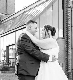A wedding couple shares an emotional embrace in an outdoor urban setting with brick buildings in the background.