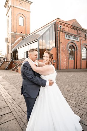 Wedding couple dancing together outside a historic brick church with arched windows and tower.