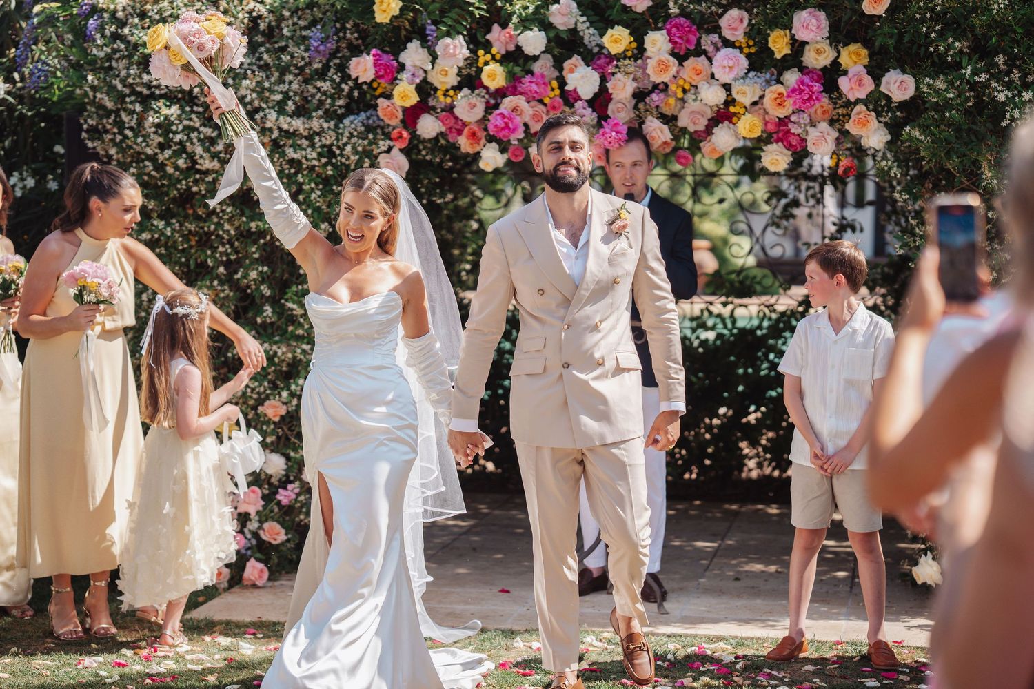 Wedding couple walking down the aisle in front of colourful flowers outdoors in finca monastario directly after their ceremony