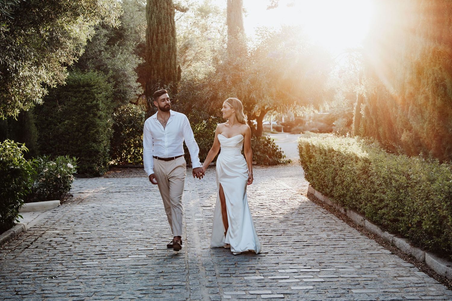 Bride and groom walk towards the camera with the sun sitting behind them smiling at one another in Finca Monastario