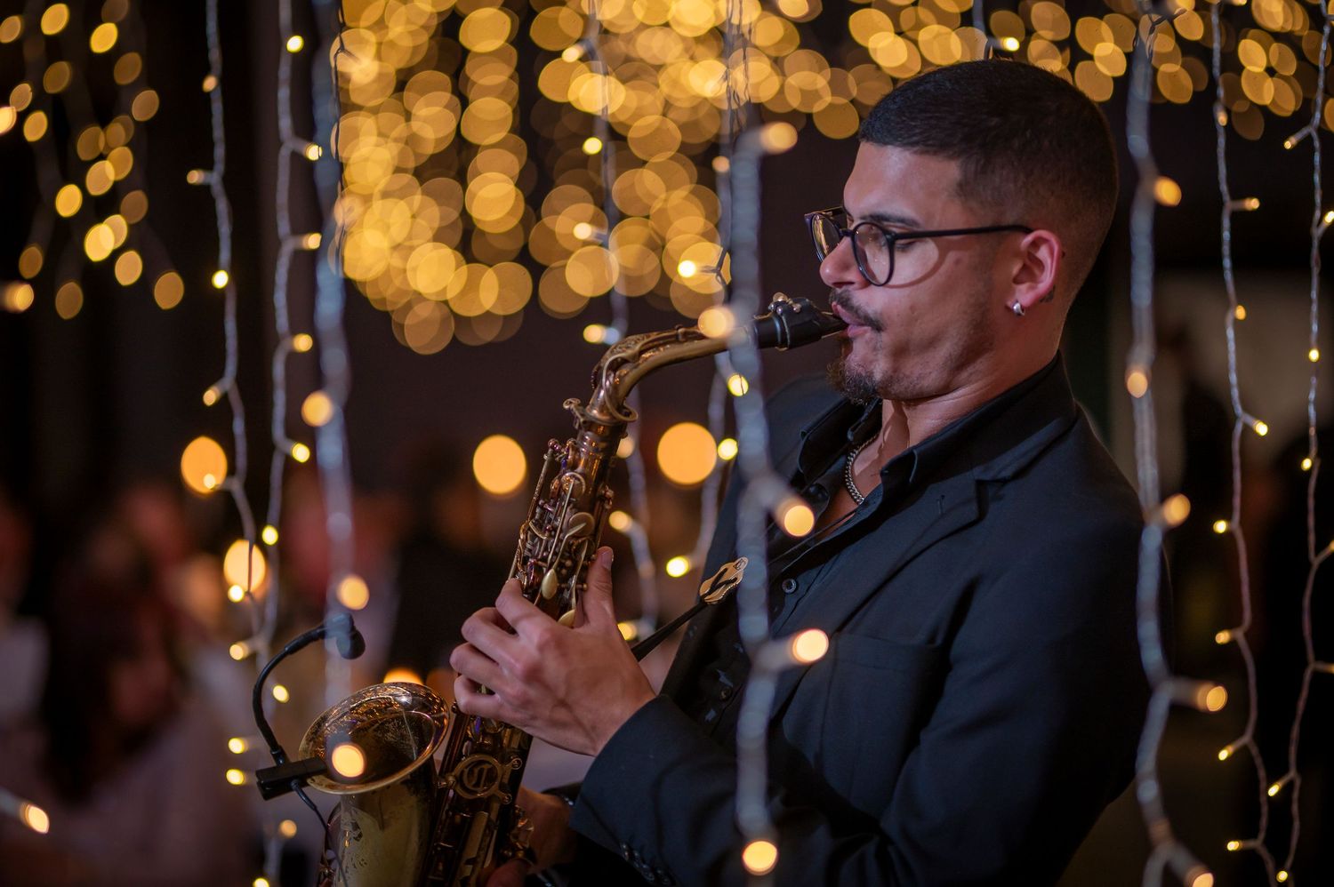 Two people sharing a romantic moment under glowing string lights at an evening celebration.