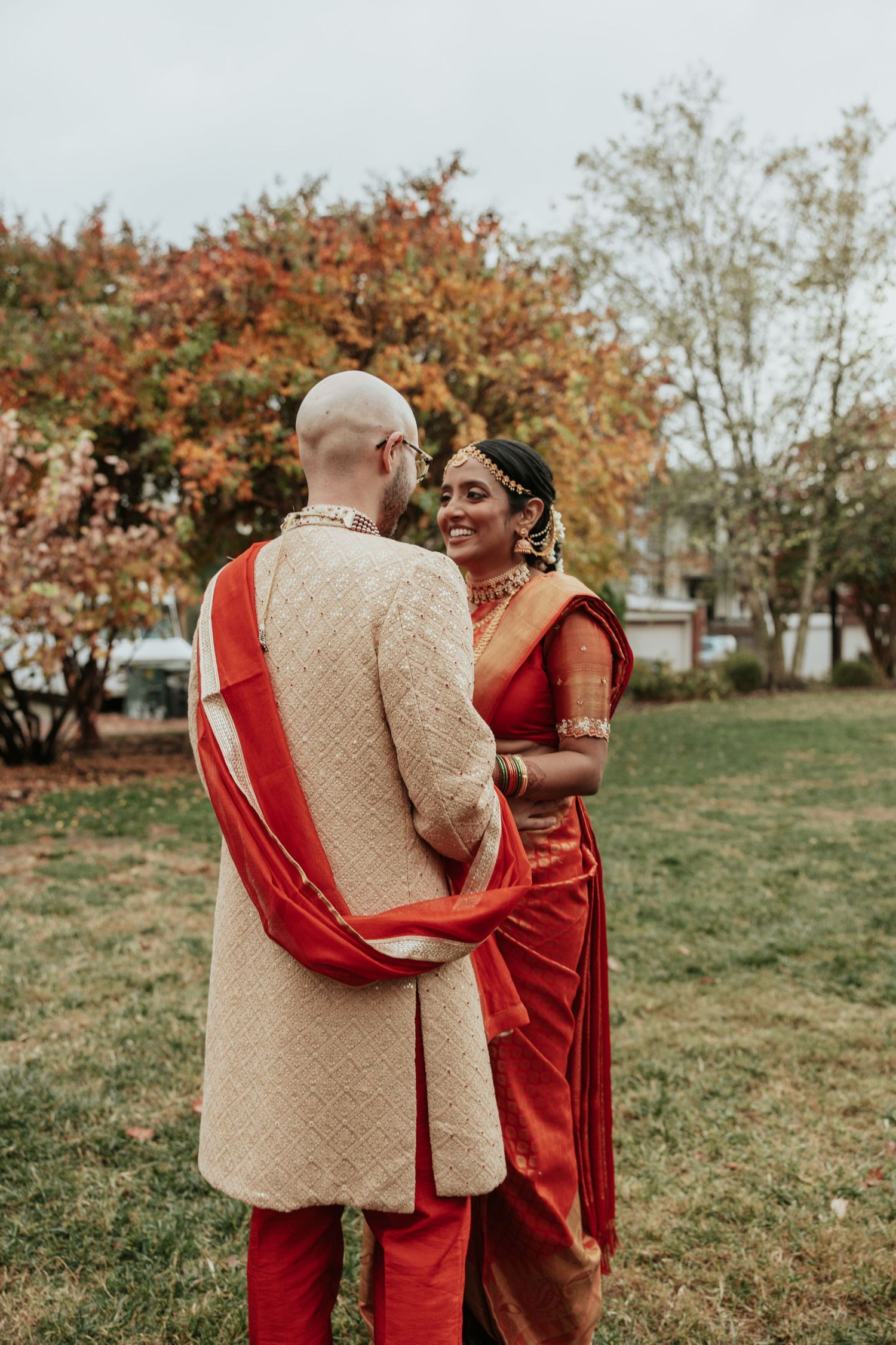 Loving couple sharing joyful moments in autumn at outdoor park while wearing coordinated red and beige outfits.