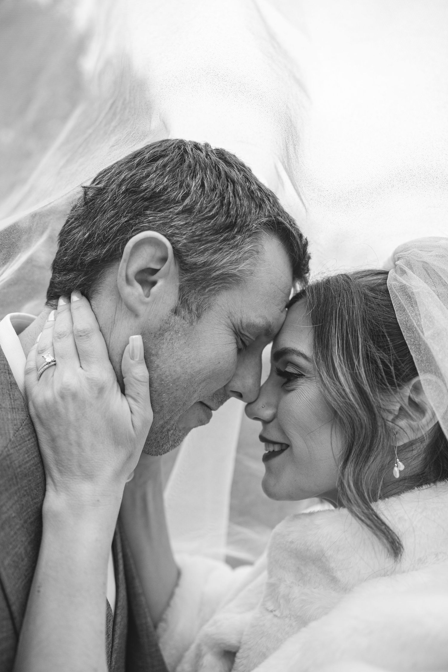 A tender black and white portrait of newlyweds sharing an intimate moment under a bridal veil.