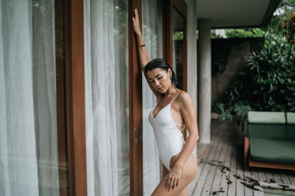 A person in white stands in an elegant indoor setting with natural light streaming through windows.