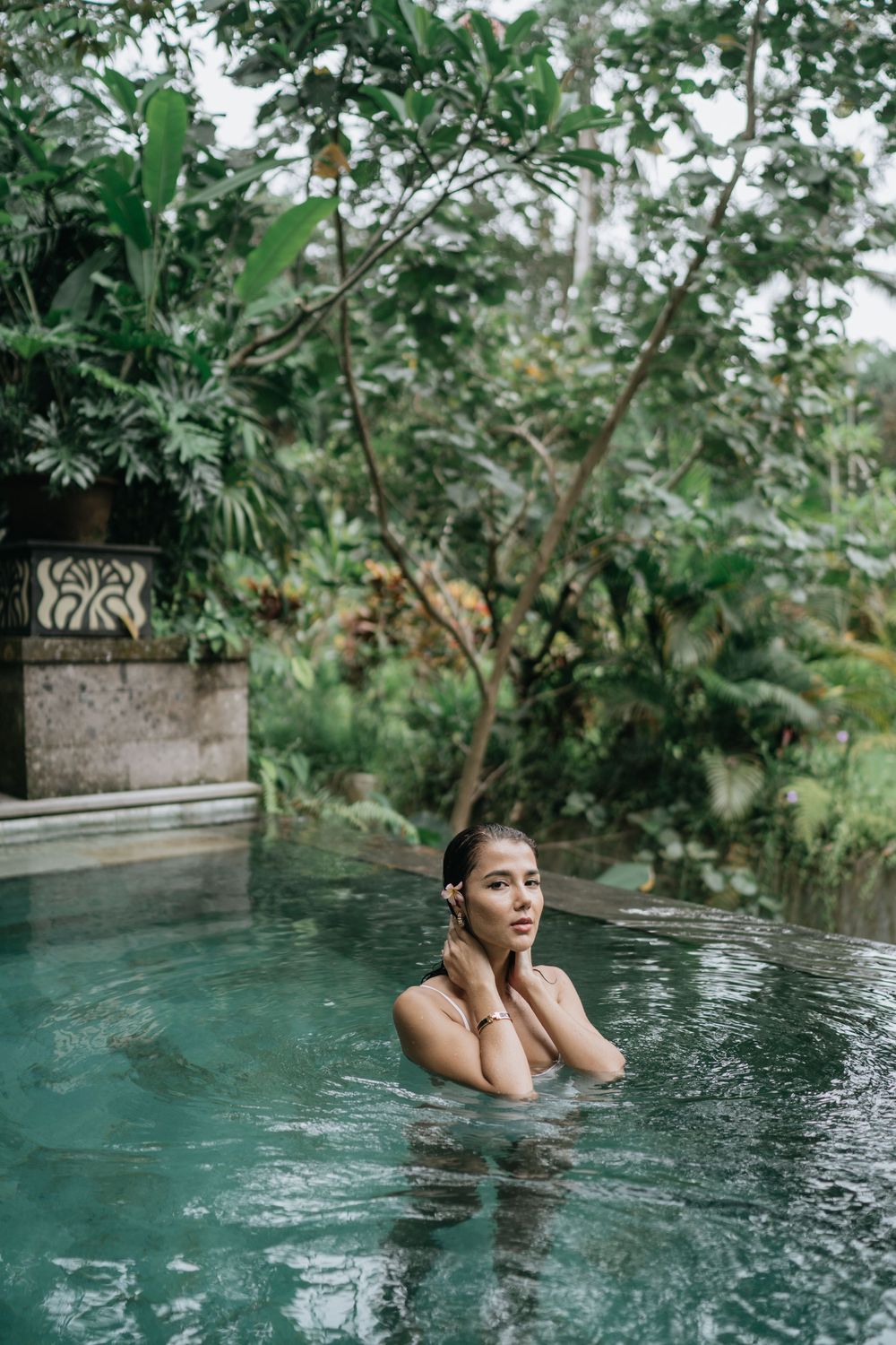 A woman relaxes in an infinity pool surrounded by lush tropical greenery.