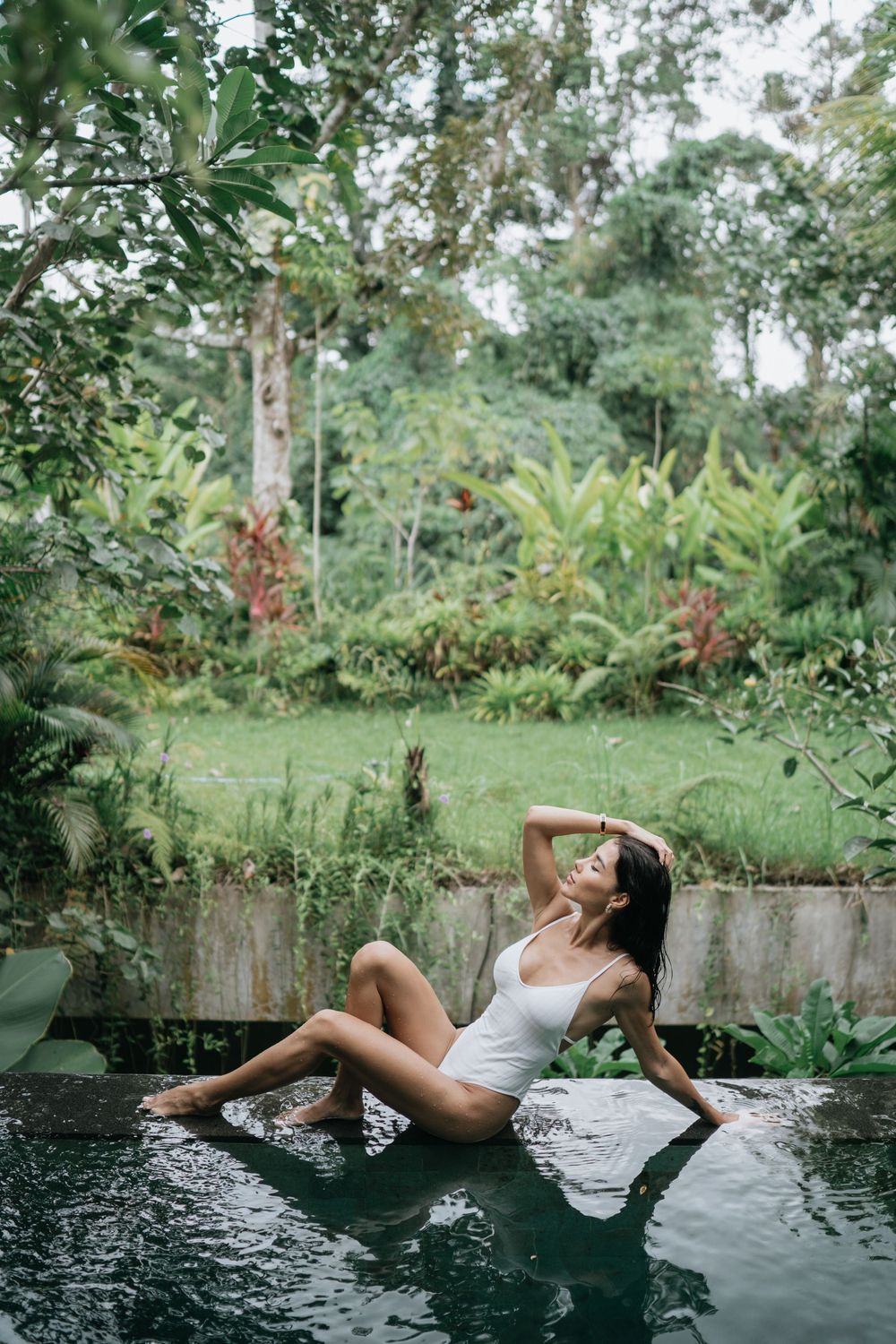 Woman relaxing in an infinity pool surrounded by lush tropical greenery at a luxury resort.
