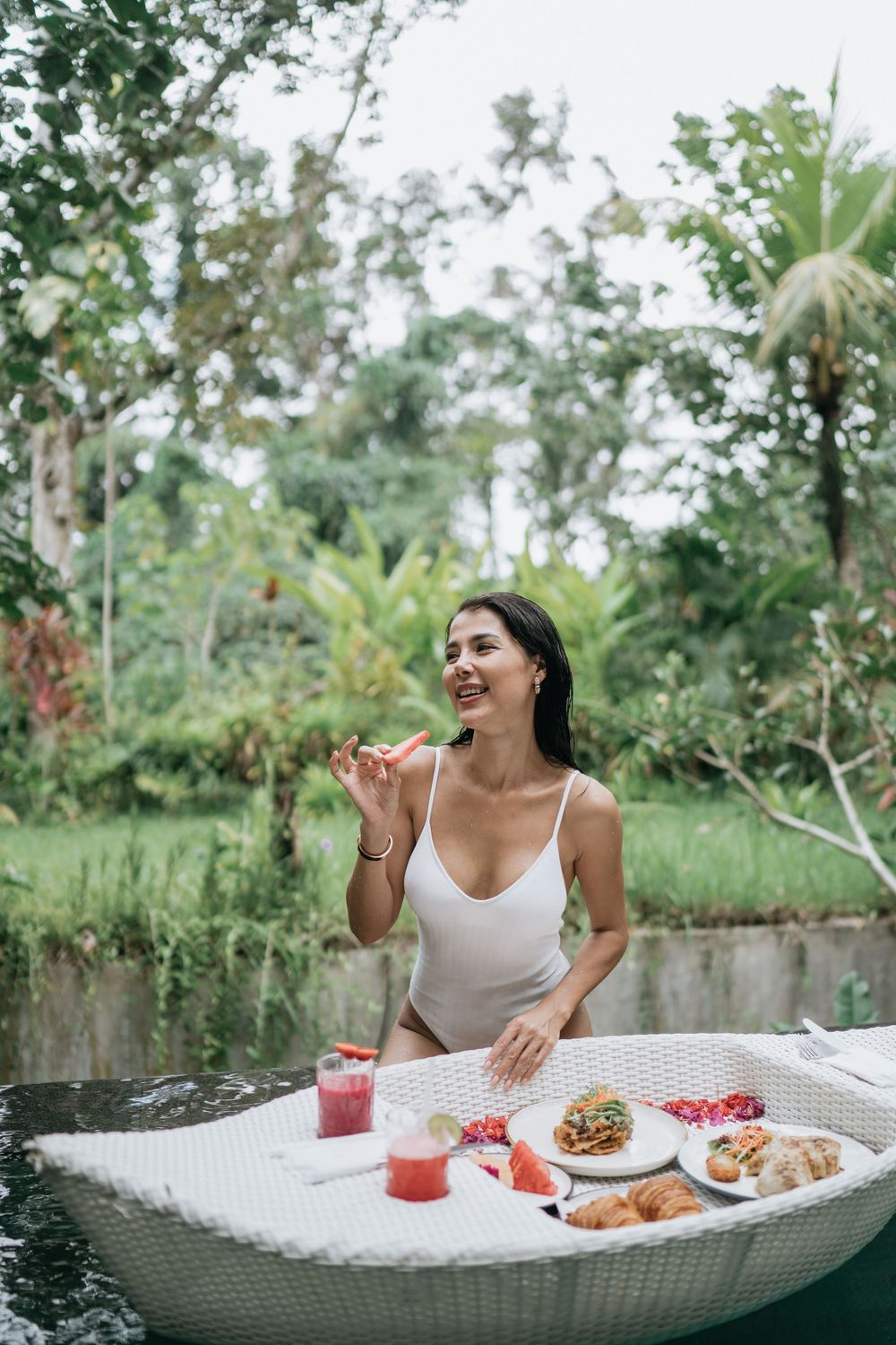 A joyful breakfast scene with tropical drinks and food on a white wicker table outdoors.